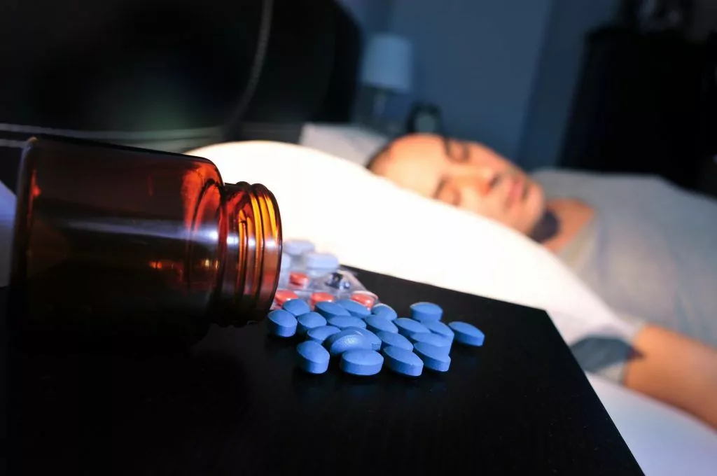 Middle aged man laying in bed sleeping with a pill pot split on his bedside containing blue tablets | This New Male Treatment Called Vidalista is Sweeping the UK, but is it Safe? | e-Surgery