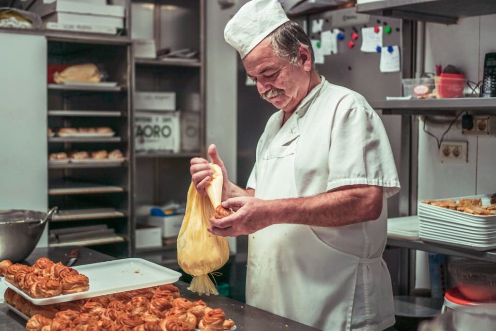 Old man in bakery with white apron moulding pastry, bakers risk occupational asthma sickness, e-Surgery