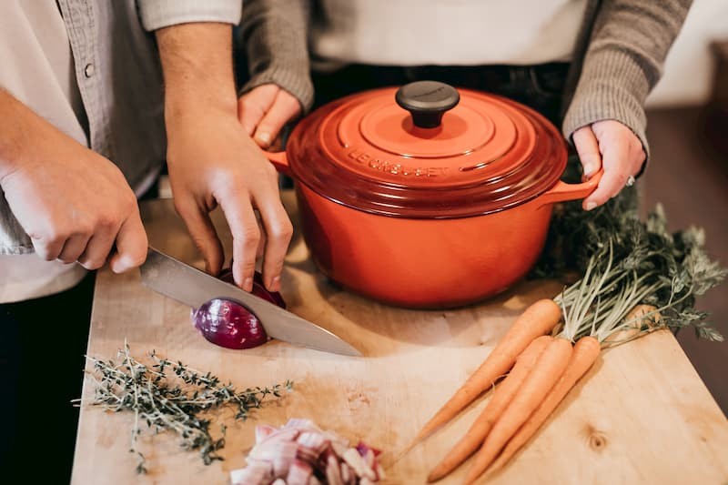 Male chopping a red onion on a brown wooden chopping boars and a female holding a crock pot | The Mental Health Survival Guide to Post-Grad Life | e-Surgery 