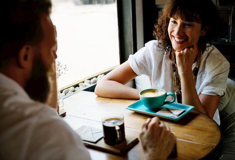 Middle aged brunette woman and man with a bear chatting over a cup of coffee  | The Mental Health Survival Guide to Post-Grad Life | e-Surgery 