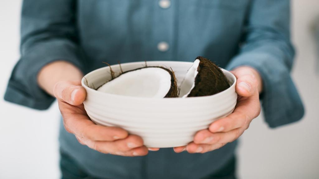 Man holding white bowl with two halves of a coconut in it, hair loss home remedies, e-Surgery