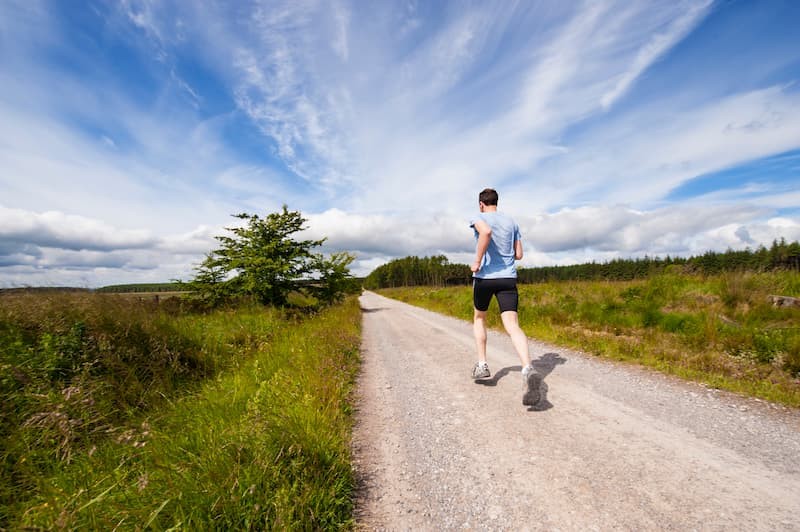 Post-grad male jogging down a country lane, it is sunny and he is wearing a blue t-shirt and cycling shorts | The Mental Health Survival Guide to Post-Grad Life | e-Surgery 