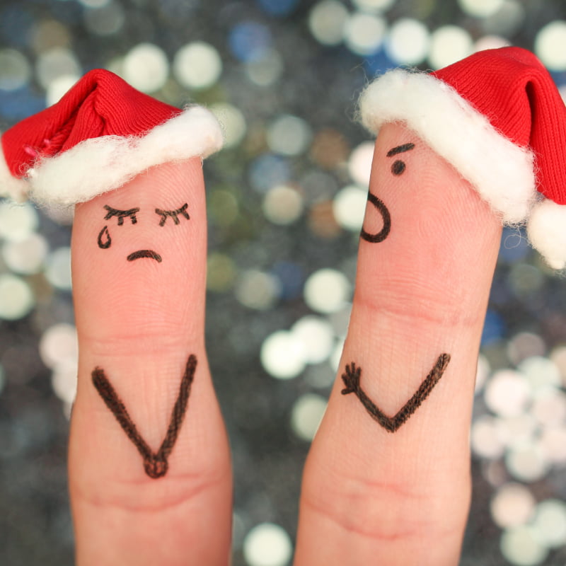 Dark side of Christmas, the tips of two fingers wearing Christmas hats. Both have faces drawn onto them, one is crying the other shouting | e-Surgery