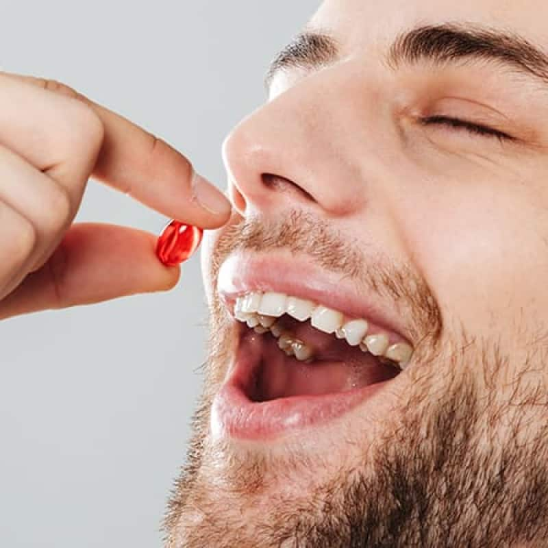 Male contraception, young male smiling and placing a red capsule pill into his mouth | e-Surgery