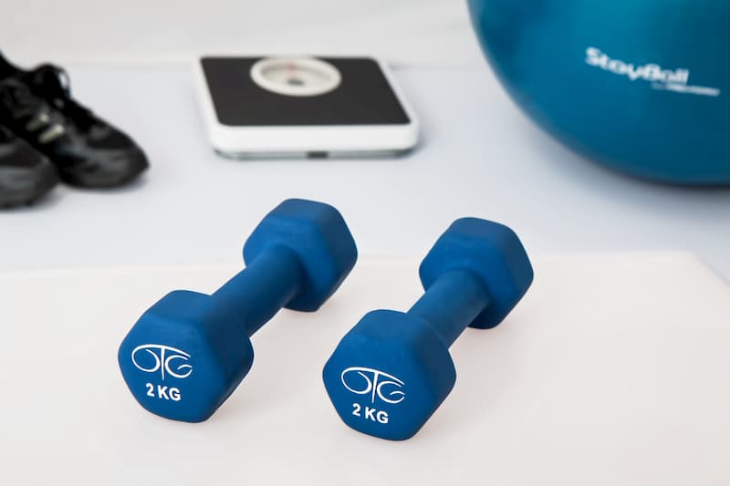 Blue small weights on table with exercise equipment in background, exercise in self isolation, e-Surgery