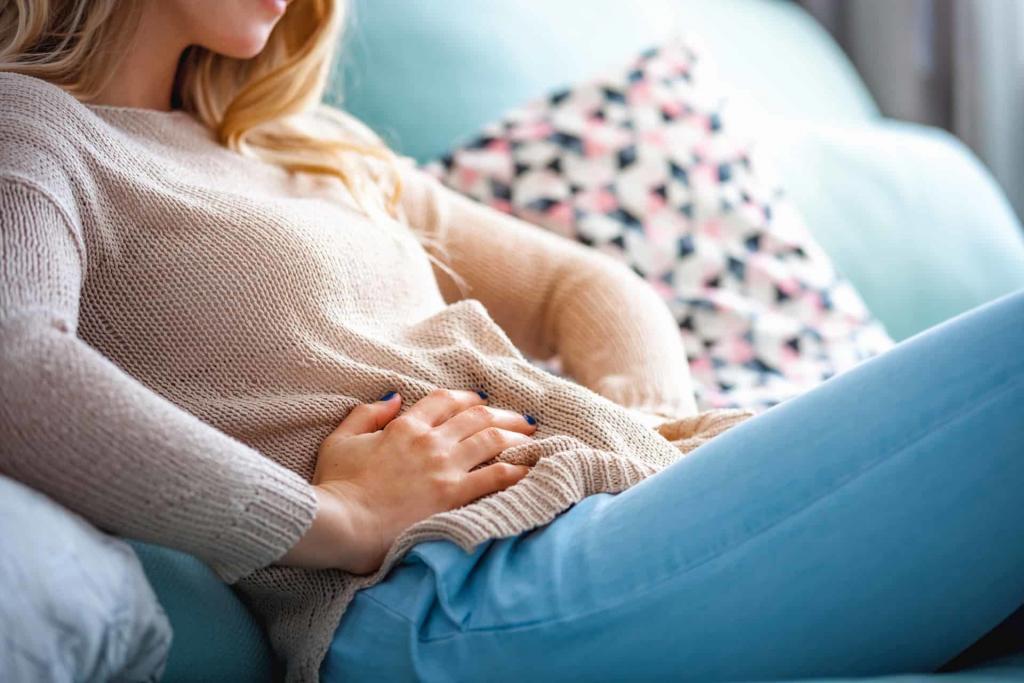 Young blonde woman on a sofa with dark blue painted nails holding her stomach | Trust Your Gut: Can Healthy Bacteria Make You Happy?  | e-Surgery 