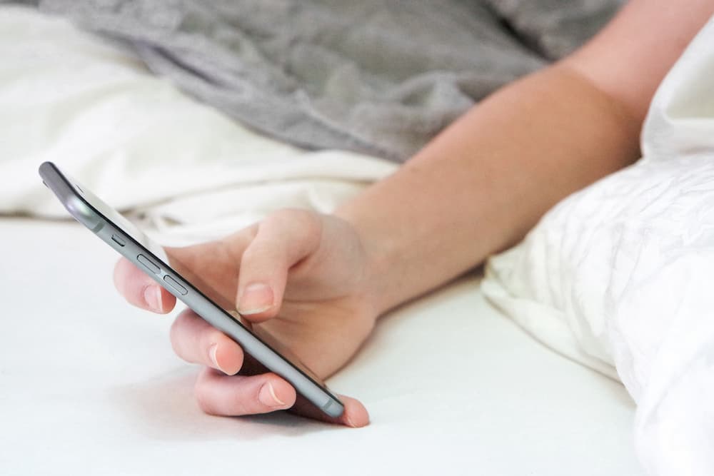 Person holding mobile phone in bed scrolling with thumb, social media in lockdown, e-Surgery