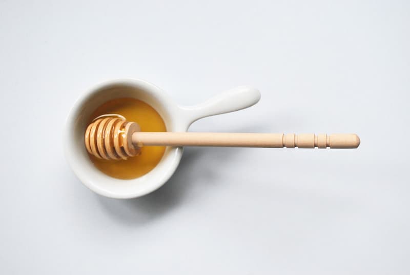 Bowl of honey with honey spoon on white table, honey home remedy for hay fever, e-Surgery