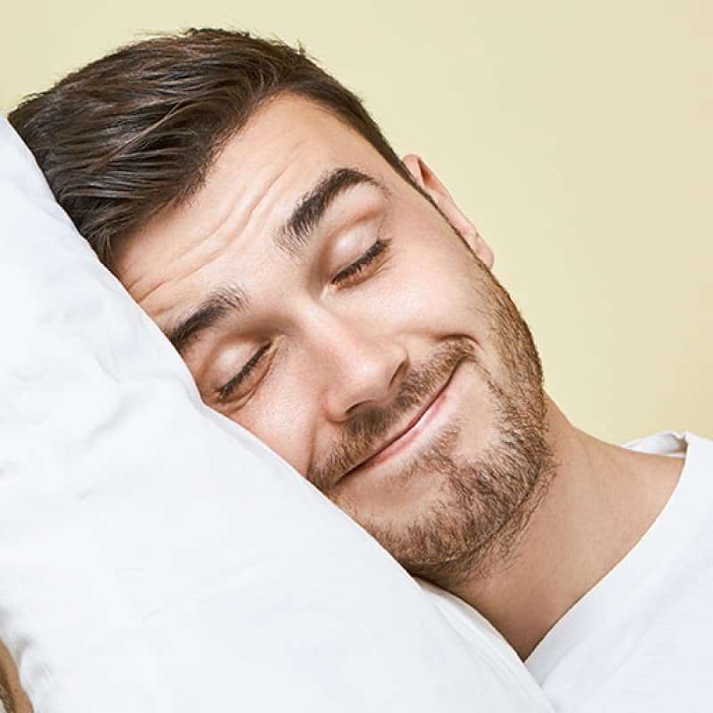 Middle aged man smiling and holding a pillow up to his head| e-Surgery