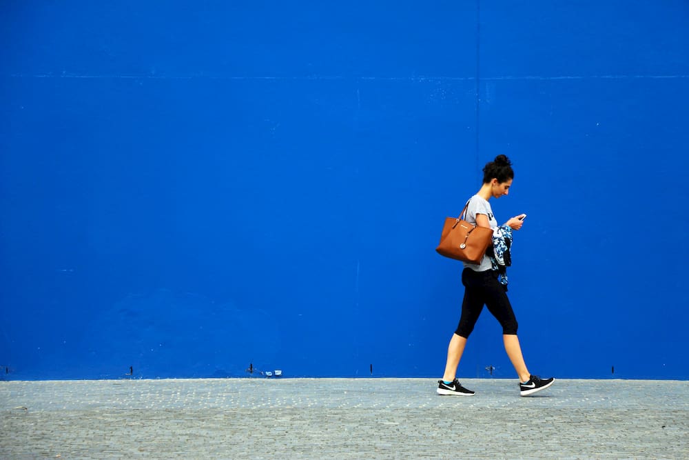 Woman walking against blue background holding mobile phone, social media in lockdown, e-Surgery