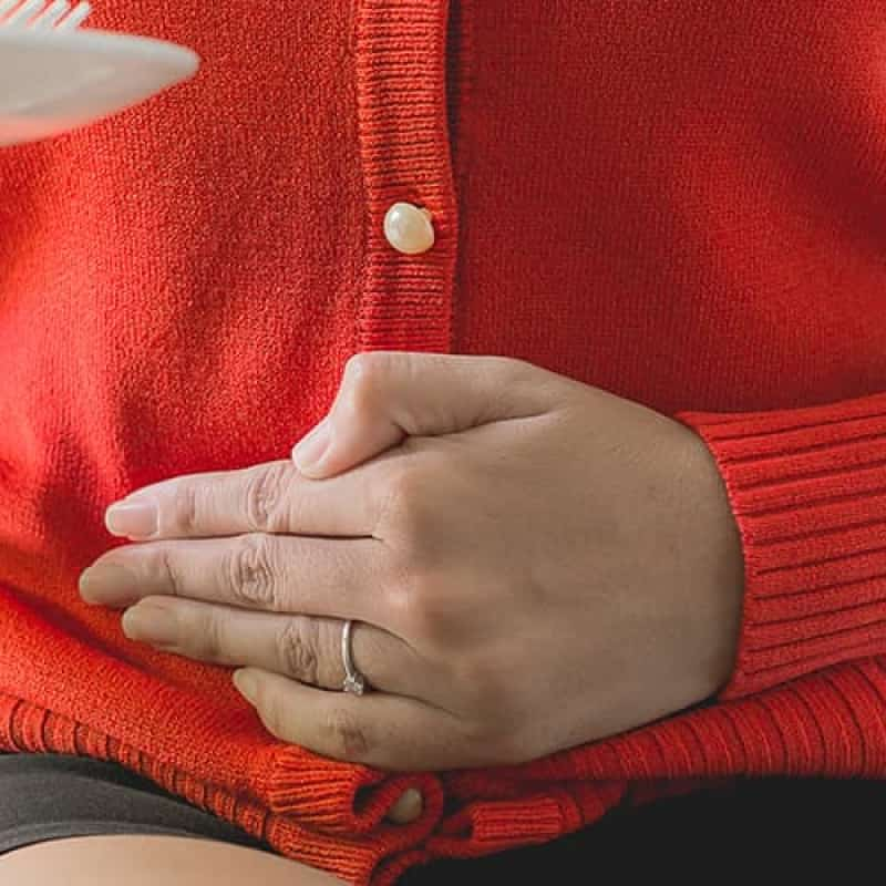 Acid reflux, Woman in a red cardigan holding a plate out and holding her stomach in pain | e-Surgery