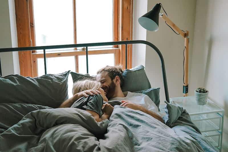 Young couple under covers cuddling in bed, talking to your partner about erectile dysfunction, e-Surgery