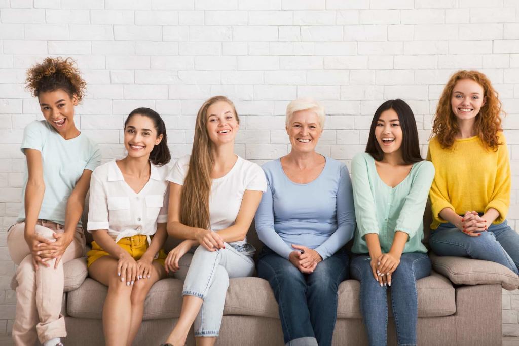 Group of women with a mixed age sitting on a sofa in-front of a white brick wall smiling at the camera | What is Bacterial Vaginosis? And Why Do Women Keep it a Secret? | e-Surgery