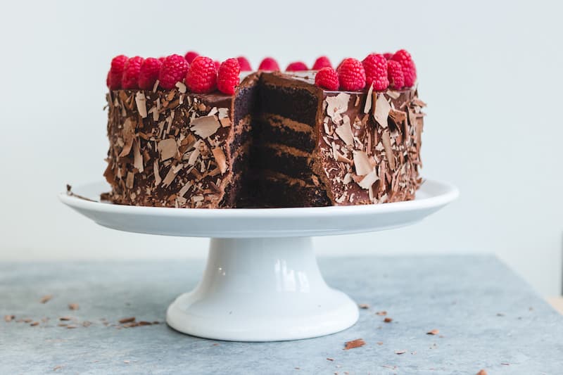 Chocolate cake on white cake stand covered in raspberries, reducing your sugar intake can reduce high cholesterol