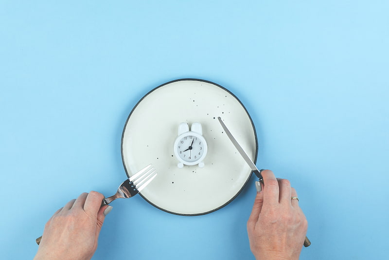 Person with a knife and fork looking like they are going to cut an alarm clock that is on a plate in half | Orlistat & Xenical:, Do weight loss pills work? | e-Surgery 