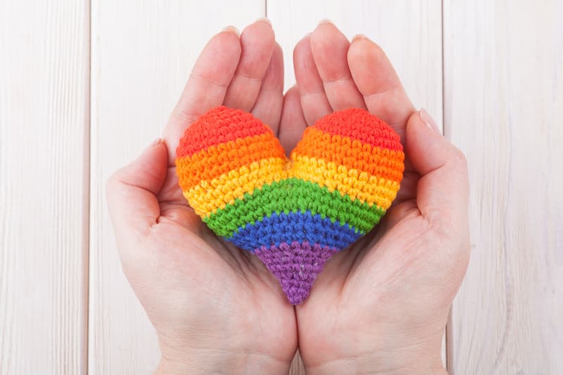 Hand holding knitter rainbow heart, LGBTQ access to healthcare at e-Surgery