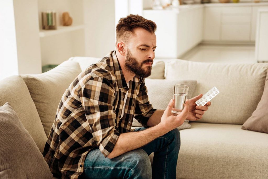 Man looking at medication and glass of water looking unsure, order effective ED treatment online at e-Surgery