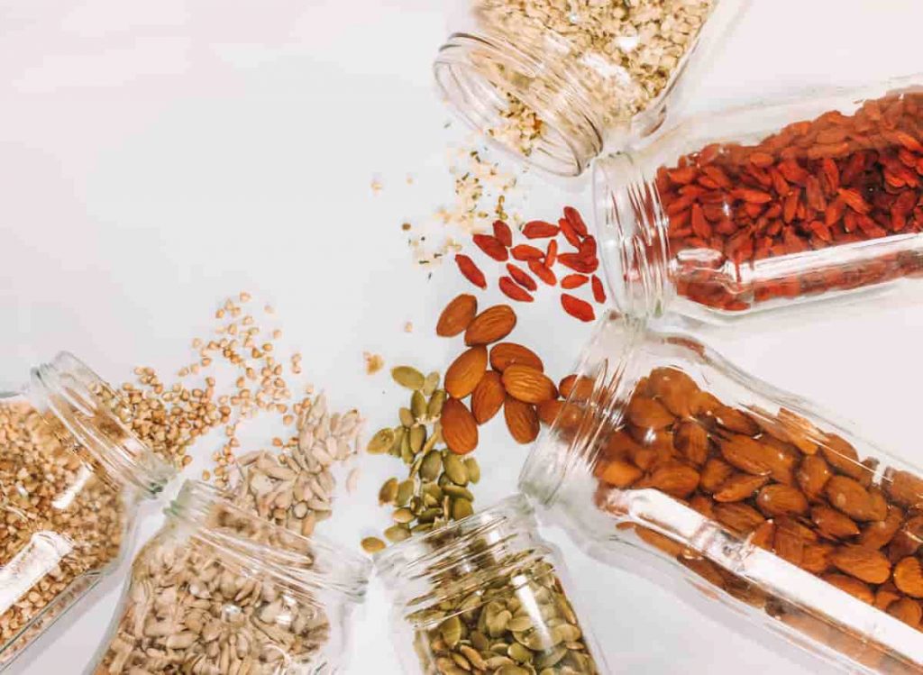 Jars of seeds and nuts laying on their side without lids. The seeds and nuts are spilling out onto the white table cloth. The image has been taken from an aerial view |  Does Your Diet Trigger Migraines? | e-Surgery  