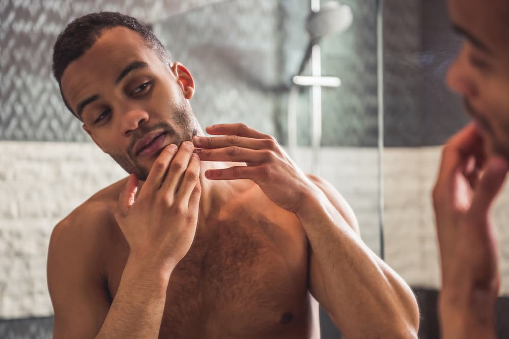 Young man touching acne looking in mirror