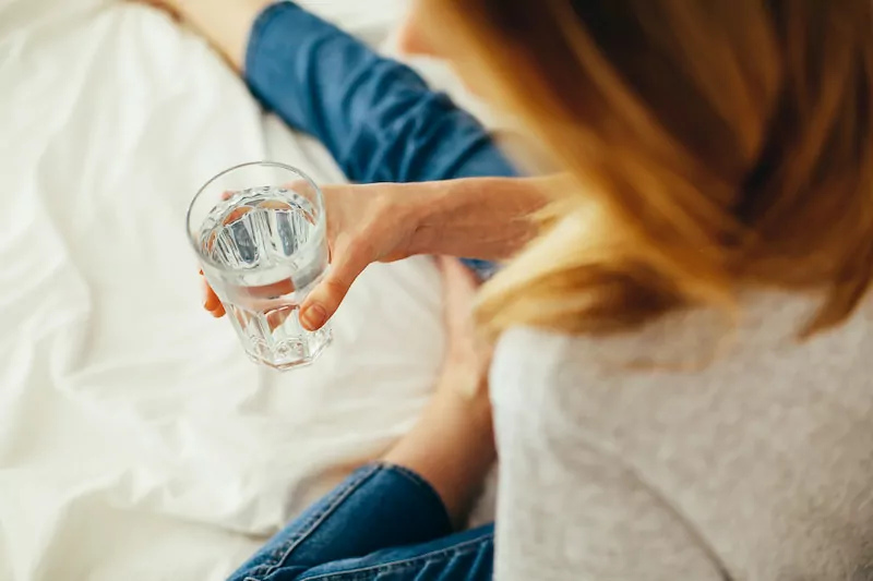 Lady holding glass of water in bed suffering with UTI pain at night