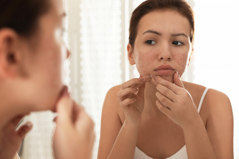 Woman suffering from acne looking in mirror