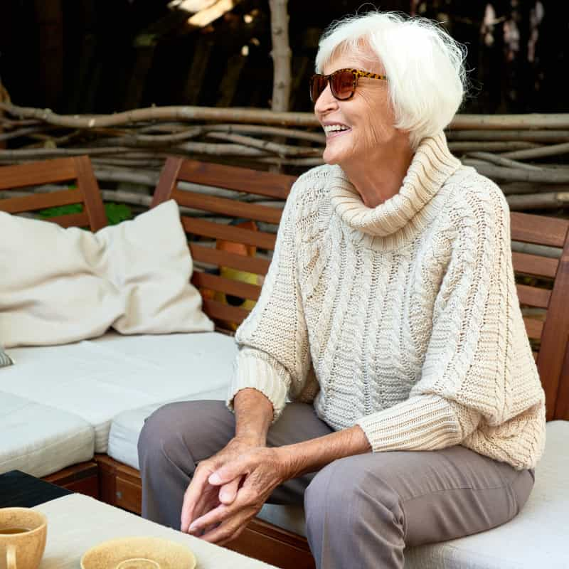 elderly woman sitting outside on a bench smiling. Heres everything you need to know about HRT | e-Surgery