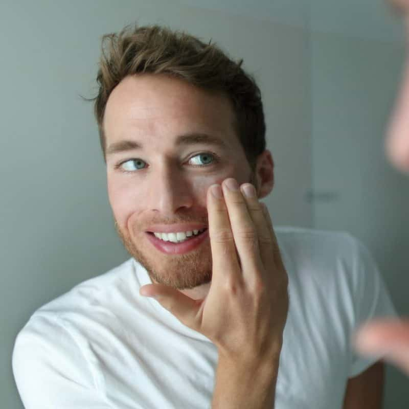 man looking at face in mirror, acne home remedies header