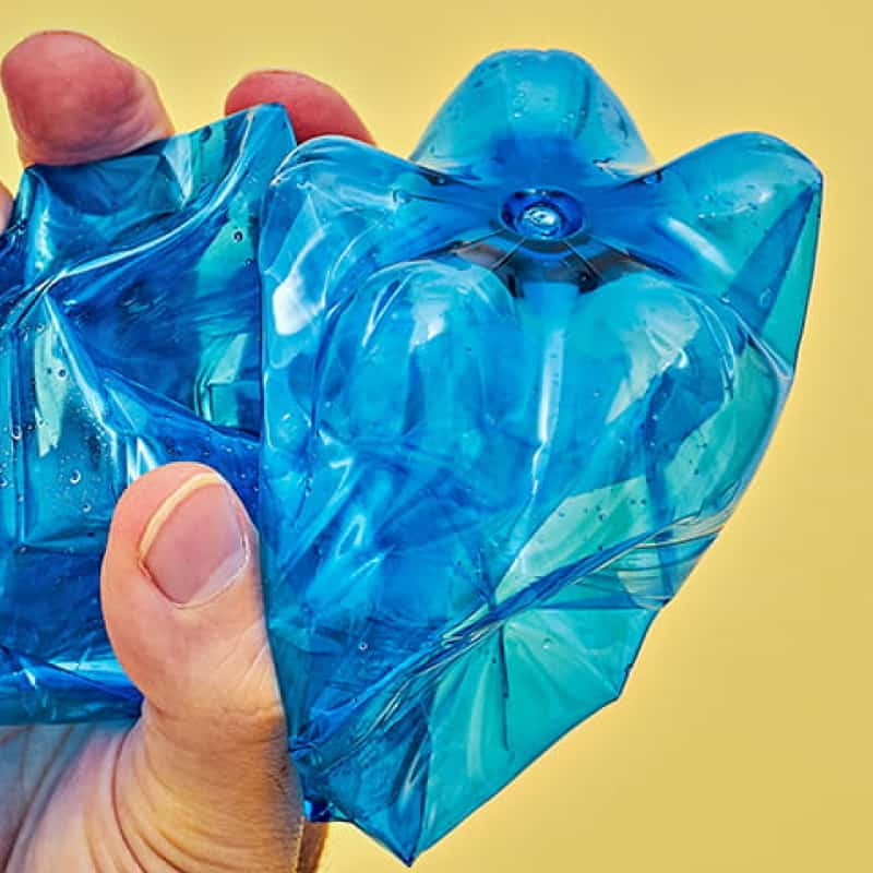 Person holding blue plastic bottle against yellow background, BPA plastic and the environment