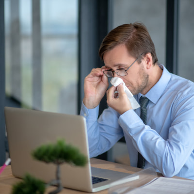 man sits at desk suffering from hayfever wondering what treatments there are for hay fever symptoms at night | e-surgery